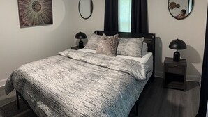 Ein Schlafzimmer mit einem Bett, zwei Nachttischen, einem Deckenventilator, einem Fenster mit Vorhängen, einem wandmontierten Spiegel und einem Wanddekor.