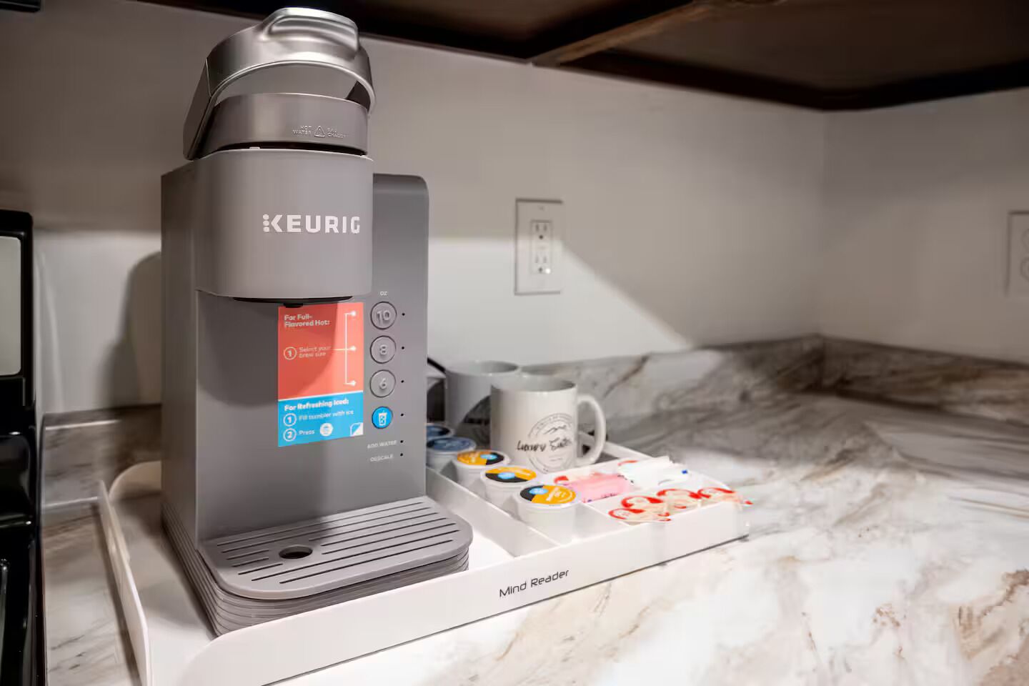 A Keurig coffee machine with a water reservoir, a mug, and a coffee pod holder on a marble countertop.