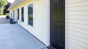 A single-story building with a dark front door, large windows, and air conditioning units on the ground floor. - Brillion 2‑Bedroom Suite w/ Full Kitchen Near Ariens – Unit #1 (Brillion)