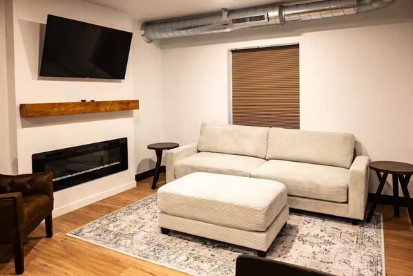 Una sala de estar moderna con un sofá, un reposapiés, chimenea, televisor y una alfombra estampada.