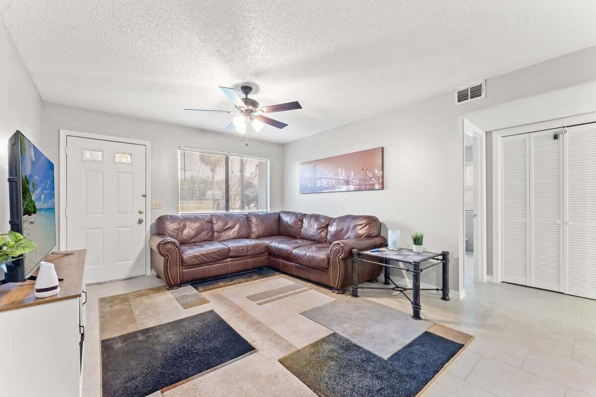 Ein Wohnzimmer mit braunem Ledersofa, Deckenventilator, Couchtisch und einem Stadtbild an der Wand.