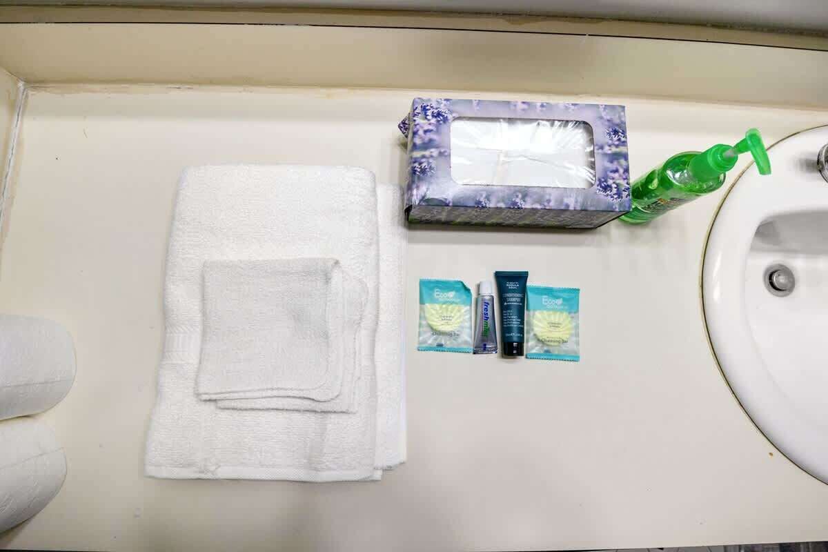 Un baño con un lavamanos blanco, una toalla blanca, un dispensador de jabón y una pequeña caja con ventanilla.
