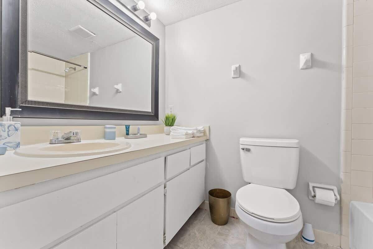 A modern bathroom with a large mirror, white fixtures, a toilet, and a trash can.