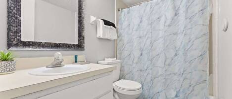 A bathroom with a white sink, a toilet, a mirror with a mosaic frame, and a shower curtain with a marble pattern.
