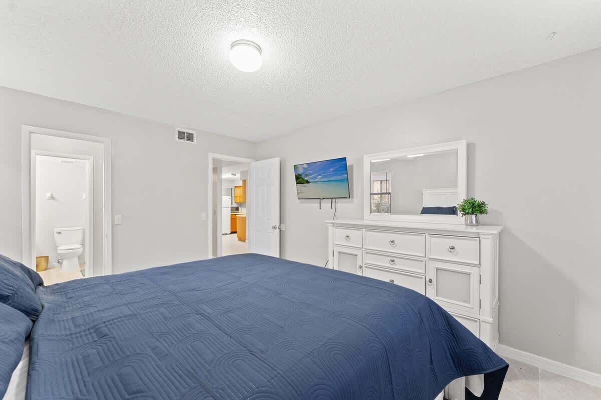 Un dormitorio con cama, cómoda, televisor y puerta que da a otra habitación.