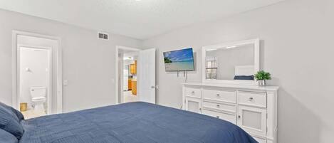 Un dormitorio con cama, cómoda, televisor y puerta que da a otra habitación.