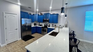A modern kitchen with blue cabinets, stainless steel appliances, and a white marble island.