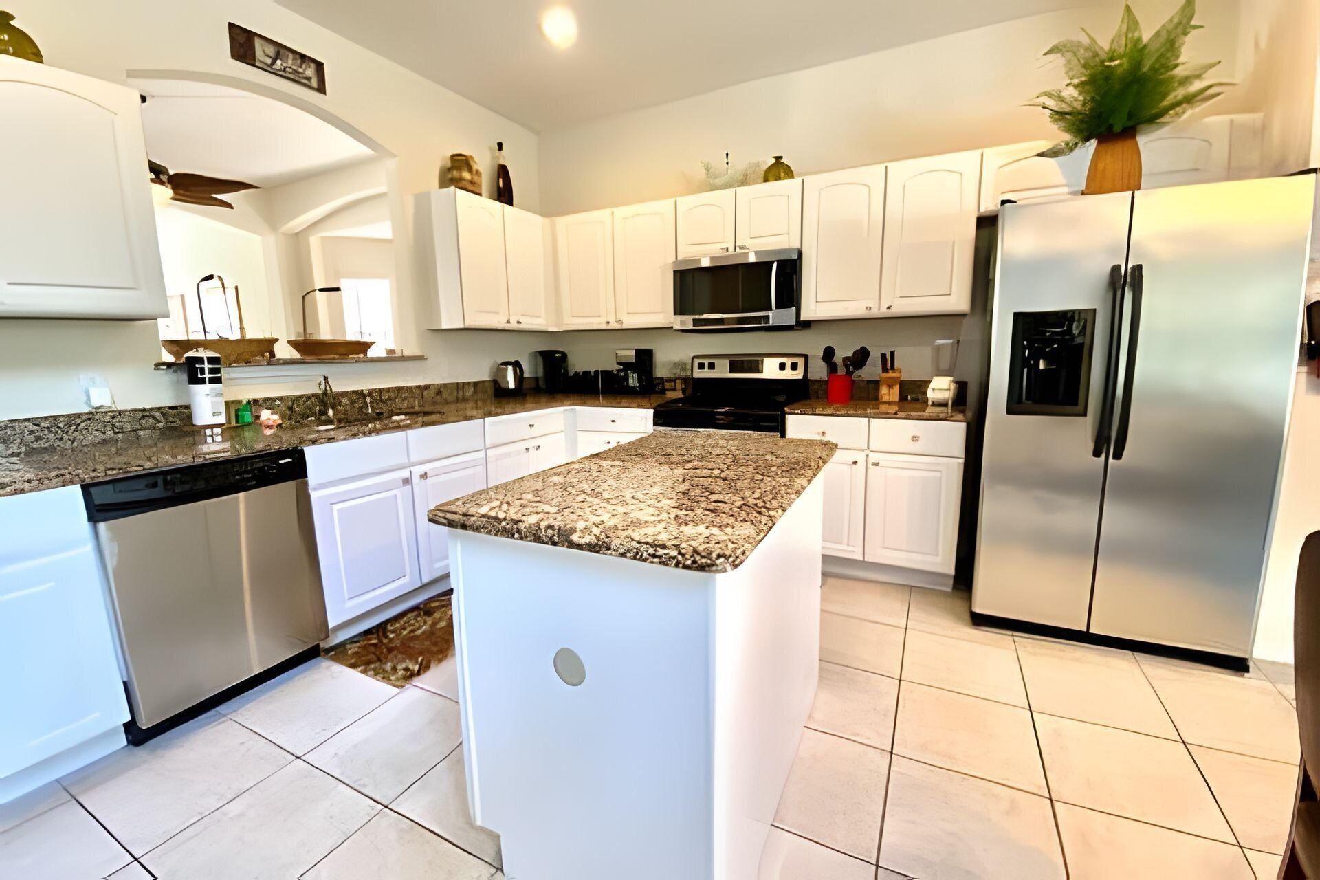 A modern kitchen with white cabinets, a granite countertop, stainless steel appliances, and a central island.