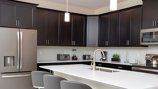 A modern kitchen with dark cabinets, a stainless steel refrigerator, a microwave, and a large island with bar stools. - 6BR Villa w/ Private Pool – Champions Gate (Four Corners)