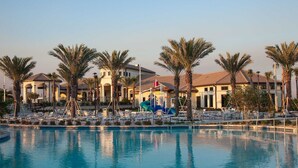 A resort pool area with palm trees, lounge chairs, and a building with a tiled roof. - 6BR Villa w/ Private Pool – Champions Gate (Four Corners)