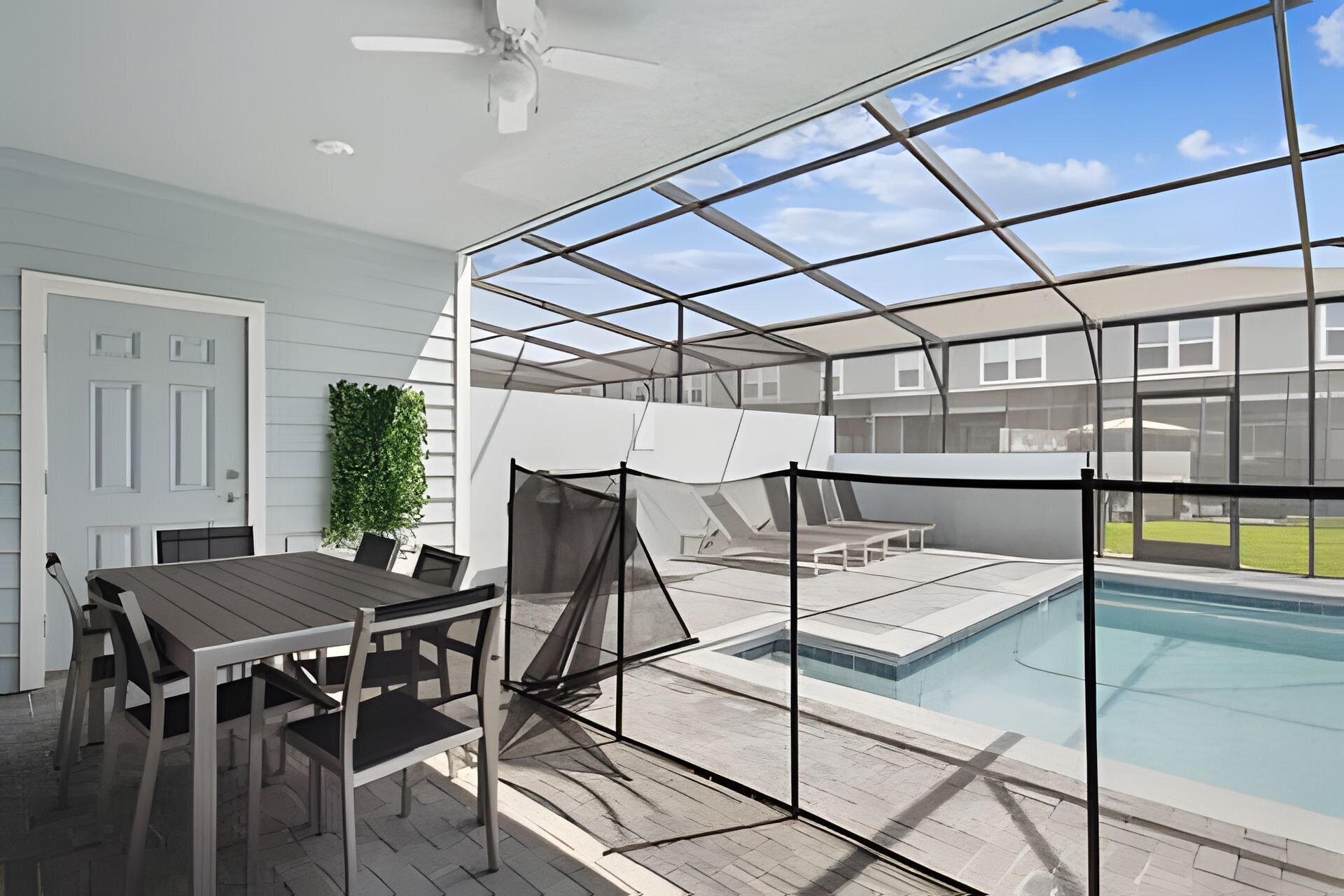A covered outdoor area with a pool, a table with chairs, and a ceiling fan.