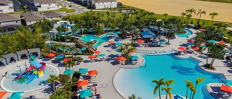 A resort with a large swimming pool, water slides, and multiple lounge areas with umbrellas.