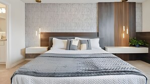 A modern bedroom with a large bed, a wooden headboard, and a built-in bench with a plant.