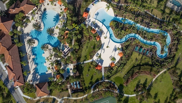 Une vue aérienne d’un complexe hôtelier doté de plusieurs piscines, de palmiers et d’une installation aquatique sinueuse.