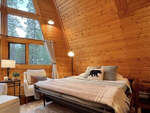 A cozy wooden cabin bedroom with a bed, bedside lamps, and a window with curtains.
