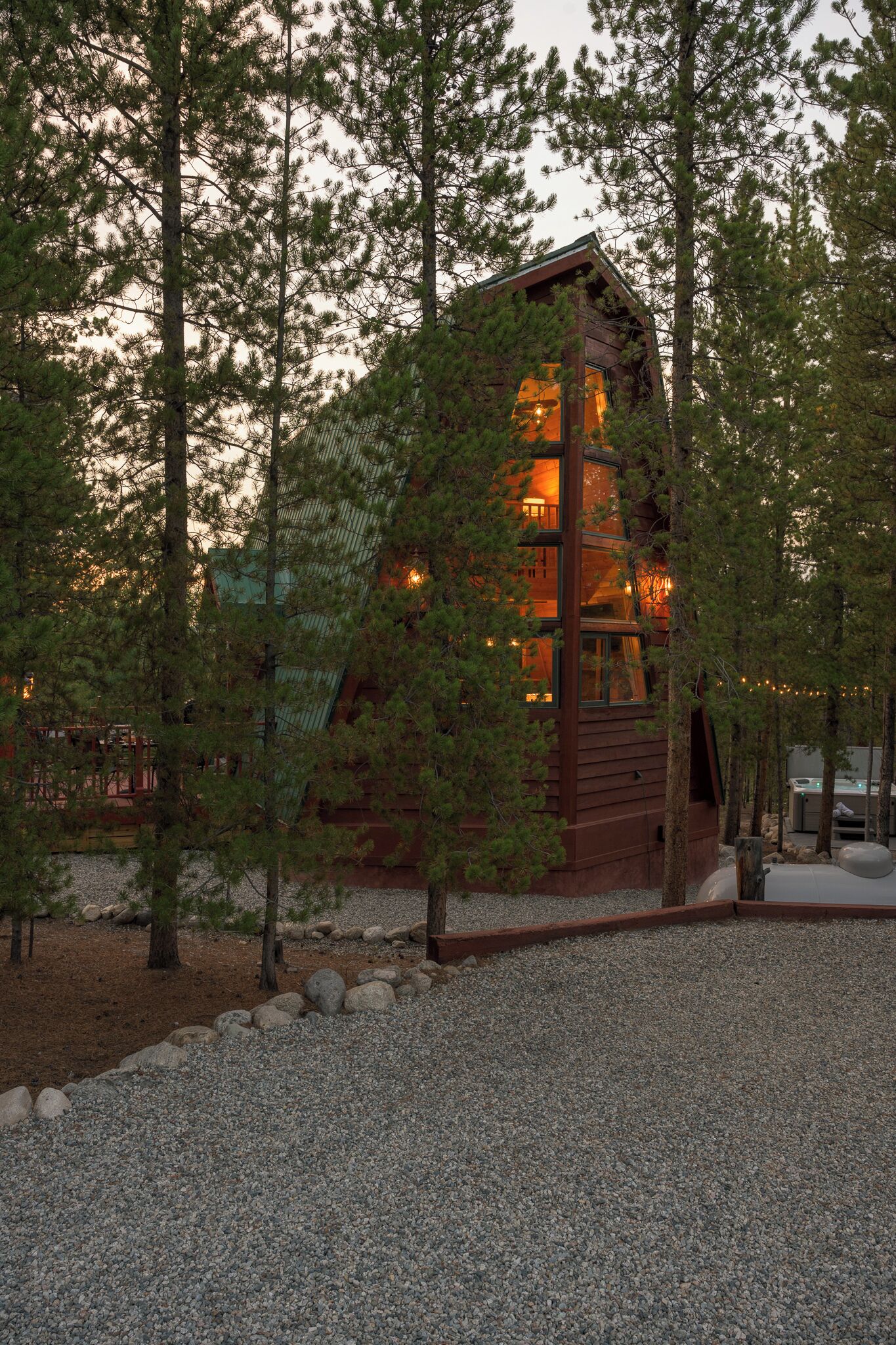 A rustic cabin with a prominent chimney, surrounded by trees and a gravel path.