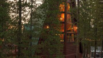 A rustic cabin with a prominent chimney, surrounded by trees and a gravel path.