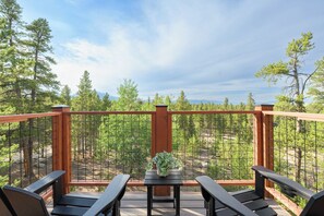 A deck with a wooden railing, a table with a potted plant, and two chairs.