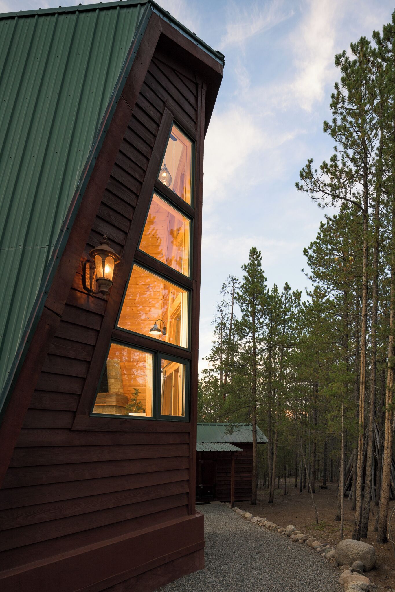 A wooden cabin with a sloped roof, large windows, and a stone foundation.