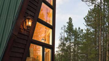 A wooden cabin with a sloped roof, large windows, and a stone foundation.