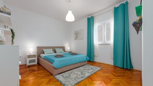 A bedroom with a bed, bedside tables, a hanging light fixture, a window with curtains, and a wooden floor. - Beautiful apartment in Preko with house sea view (Preko)