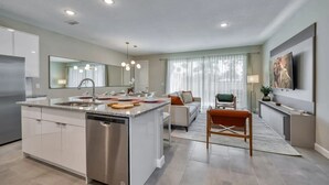 Une cuisine moderne avec un îlot central, un coin repas avec un canapé et un téléviseur fixé au mur.