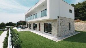 Una casa moderna de dos pisos con fachada de piedra, amplias ventanas y un césped bien cuidado.