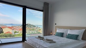 Una habitación de hotel con una cama grande, vistas a un pueblo costero y una puerta corrediza de cristal.