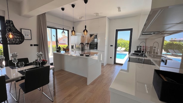 Una cocina moderna con una isla central, comedor con sillas y vista a una piscina.