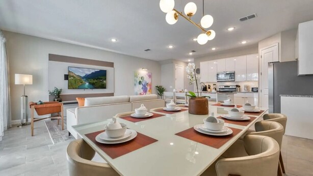 Un espace de repas moderne avec une longue table dressée pour six personnes, un canapé et une cuisine en arrière-plan.