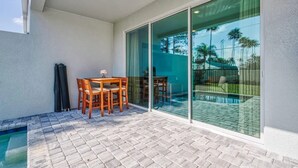 Une terrasse avec une table et des chaises, une porte vitrée donnant sur un espace piscine et une petite piscine.