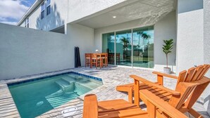 Un espace piscine extérieur moderne, doté d’un jacuzzi, de chaises longues en bois et d’une porte vitrée donnant sur un patio.