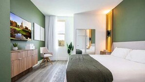 A modern hotel room with a large bed, a desk, a chair, a wardrobe, and a large window.