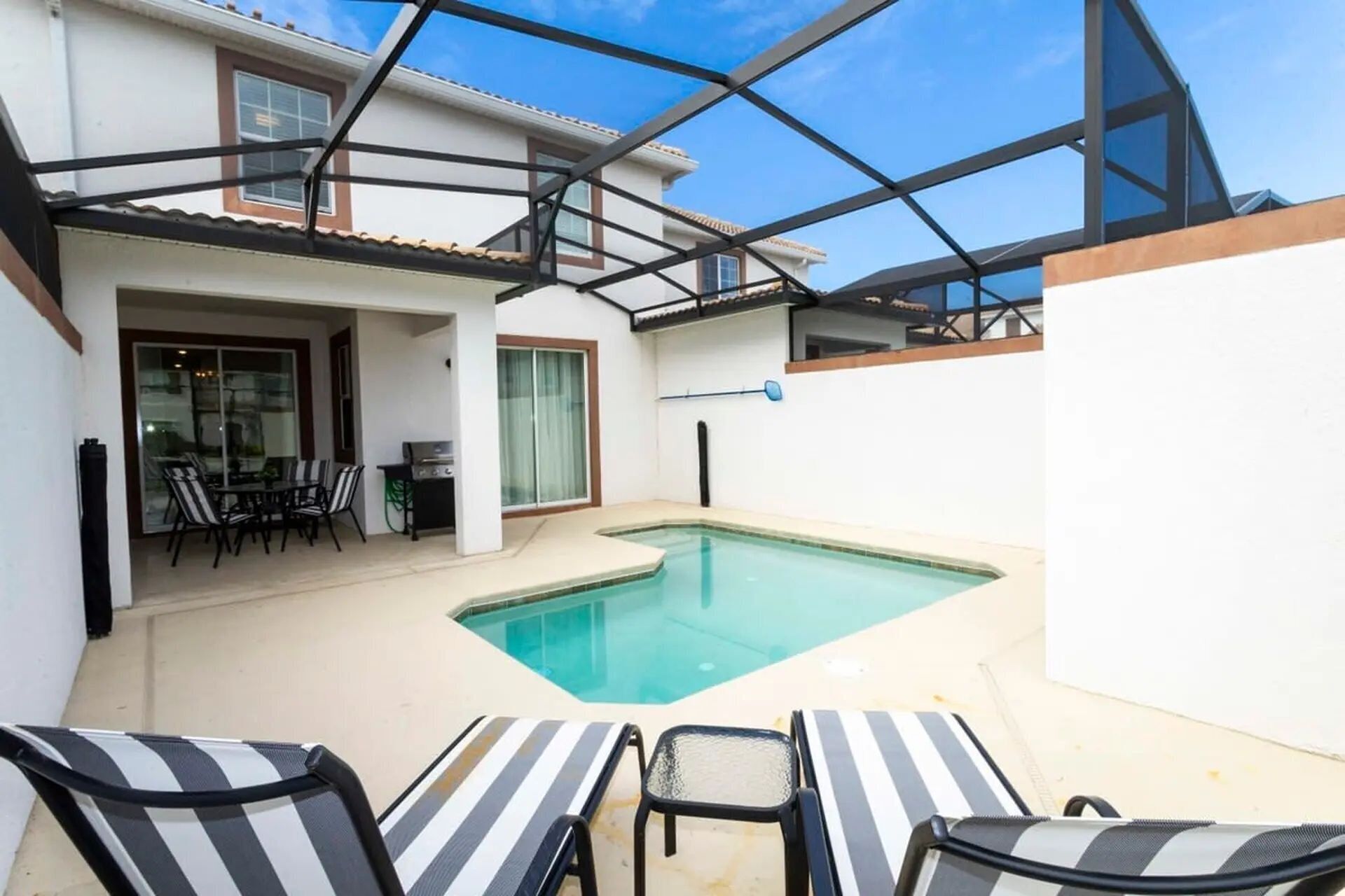 Un área de piscina con techo de vidrio, una mesa de comedor con sillas y una parrilla.