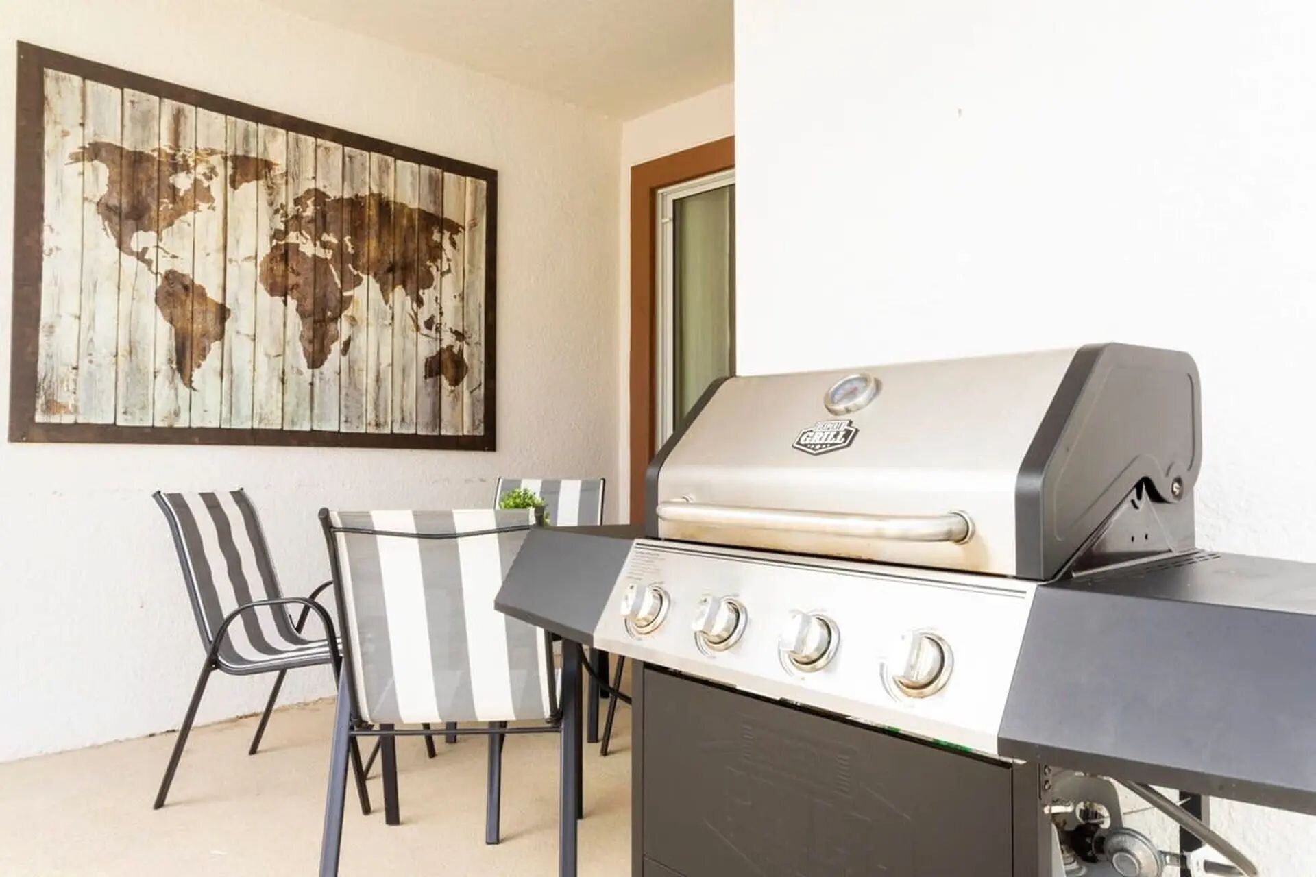 Eine Terrasse mit Grill, zwei Stühlen und einer Weltkarte als Wandbild.