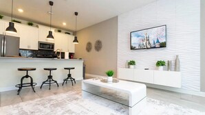 A modern kitchen with a central island, bar stools, pendant lighting, and a flat-screen TV on the wall. - 4BR Home with Private Pool & Disney Themes (DAVENPORT)