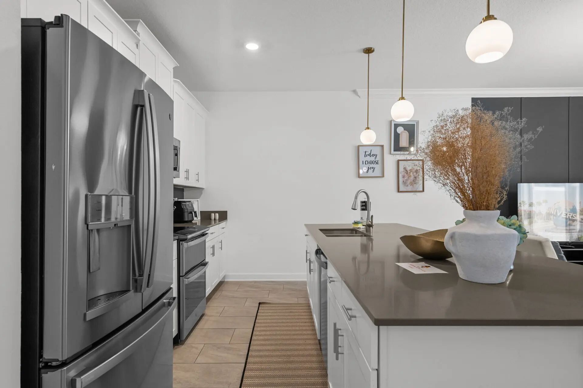 A modern kitchen with stainless steel appliances, a central island, pendant lighting, and a view of the city through a window.