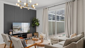 Una sala de estar moderna con un televisor de pantalla plana, una mesa de centro redonda de madera y un sofá gris.