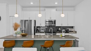 Una cocina moderna con armarios blancos, electrodomésticos de acero inoxidable y una isla central con taburetes de bar.