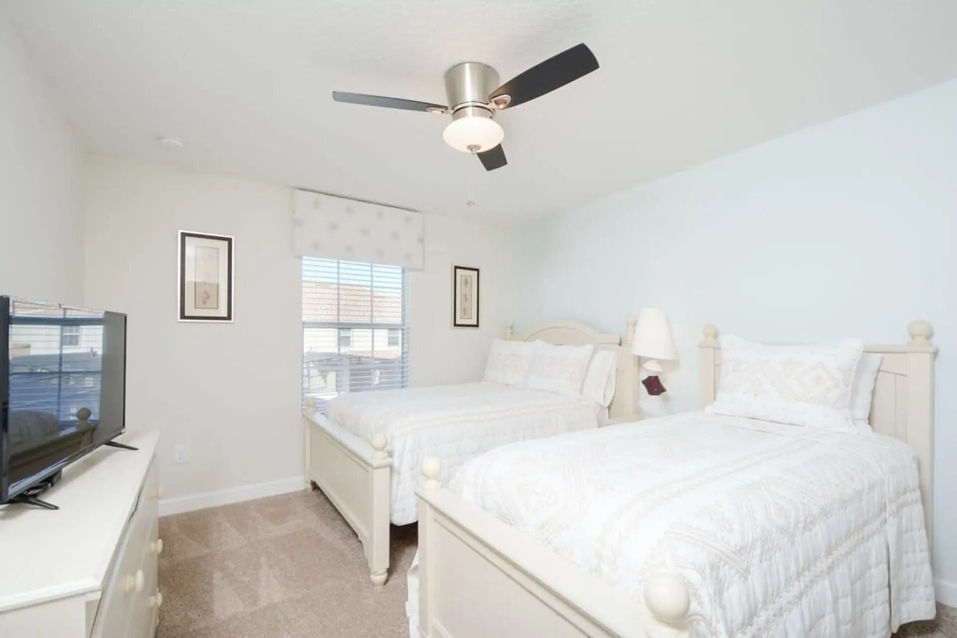 A bedroom with two beds, a ceiling fan, a television, and a window with blinds.