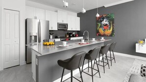 Una cocina moderna con armarios blancos, una isla central con taburetes altos, un microondas y un cuadro grande de Mickey Mouse en la pared.