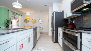 A modern kitchen with white cabinets, stainless steel appliances, and pendant lighting.