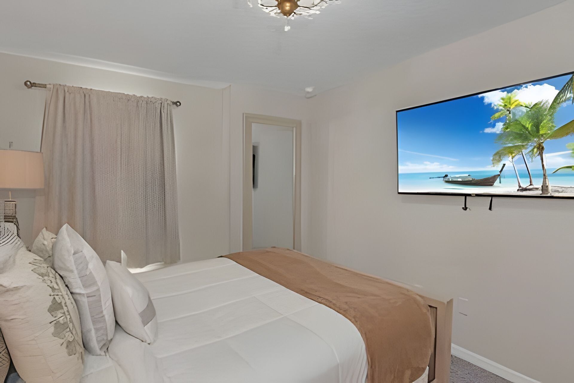 Un dormitorio con una cama, un televisor en la pared, una puerta y una ventana con cortinas.
