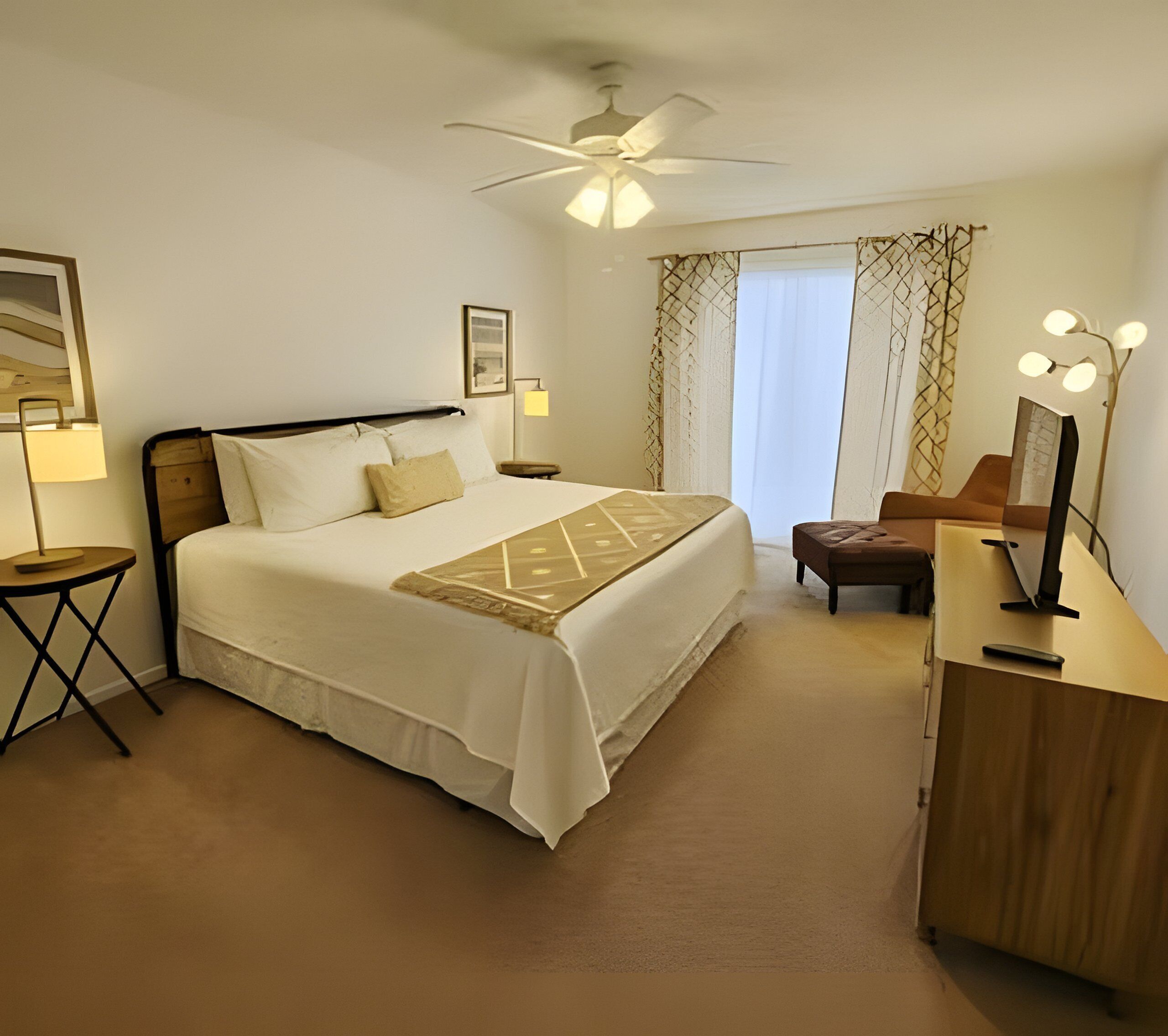 Habitación de hotel con cama, lámparas de noche, escritorio con espejo y ventilador de techo.