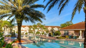 A pool area with palm trees, lounge chairs, and a building with a tiled roof. - Cozy 3BR Home Near Disney & Outlets (Kissimmee)