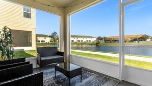 A sunlit patio with wicker furniture, a glass table, and a view of a lake and buildings in the distance. - Cozy 3BR Home Near Disney & Outlets (Kissimmee)