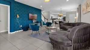 A modern living room with a blue accent wall, a grey sectional sofa, and a round coffee table. - Cozy 3BR Home Near Disney & Outlets (Kissimmee)