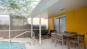 A modern outdoor pool area with a glass table and chairs, a yellow wall, and a view of trees. - Beautiful Retreat *5min -> Disney *Pool *King Bed (Kissimmee)