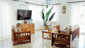 Un salon avec un téléviseur, des meubles en bois, une grande plante et une fenêtre avec des rideaux.