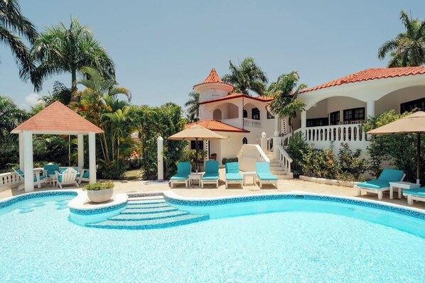 A resort with a swimming pool, lounge chairs, and a gazebo.